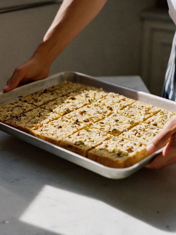 A tray of freshly baked pistachio traybake being lifted onto a marble worktop